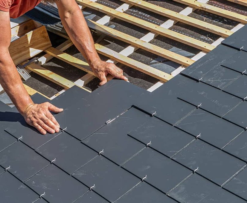 Roofer installing dark roof tiles on wood framing
